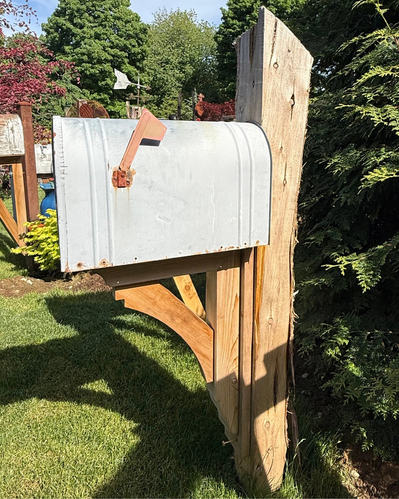 Side view of a vintage XL mailbox mounted on a handcrafted cedar post with decorative curved support bracket and rustic detailing.