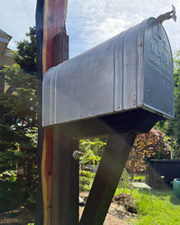 Angled close view of a vintage XL mailbox with red flag mounted on a handcrafted cedar slab post reinforced with steel.