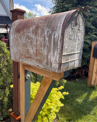 Close angled view of a weathered vintage mailbox mounted on a handcrafted cedar and steel support structure with rustic character.