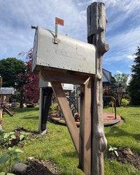 Angled view of a rustic mailbox set featuring a weathered cedar log post, handcrafted cedar support bracket, and vintage-style XL mailbox.